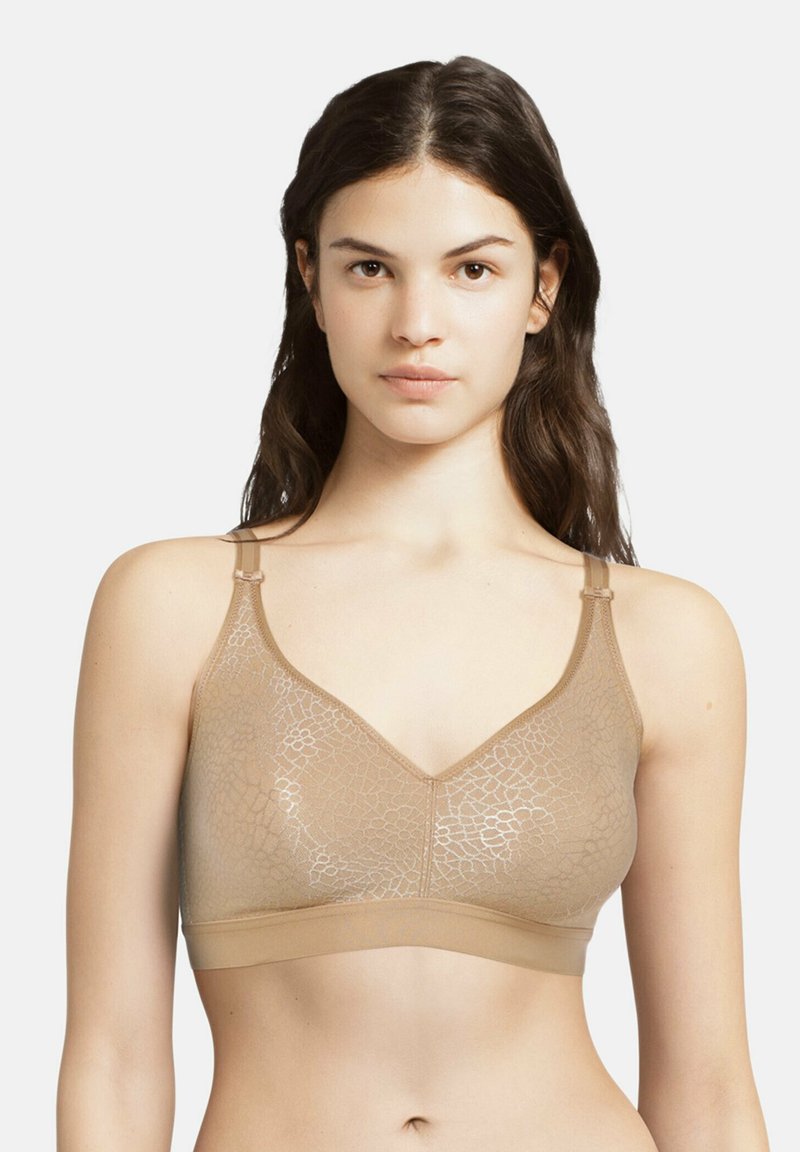 Beige wireless bra with a textured, semi-sheer lace pattern. Features adjustable straps and a V-neck design for comfortable fit.