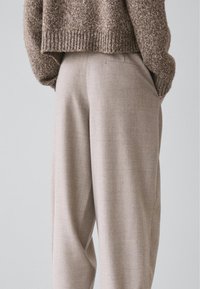 Lyse beige bukser med en afslappet pasform, lavet af et tekstureret stof. Bukserne har sidelommer og et diskret mønster.