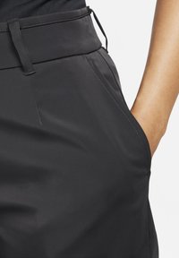 Pantalones negros con una textura lisa, que cuentan con una cintura plana, bolsillo lateral y costuras precisas a lo largo de las costuras.