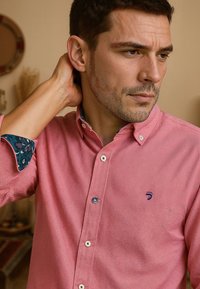 Lichtroze knoopshirt van textuurstof. Heeft contrasterende gebloemde manchetten in donkerblauw en een klein logo op de borst.