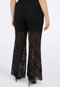 Zwarte kanten flared broek met doorschijnende onderbenen, voorzien van bloemmotieven en een gestructureerde afwerking. Ontworpen met een aansluitende taille.