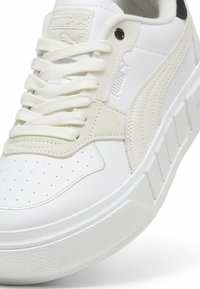 Baskets blanches avec une tige en cuir lisse, des accents en suède, un motif perforé sur le bout et une semelle en caoutchouc texturé et épais.