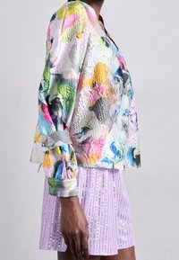 Colorful, textured jacket with a mix of pink, green, and blue hues. Features long sleeves, cuffed ends, and a cropped cut. Paired with a light purple sequined skirt.