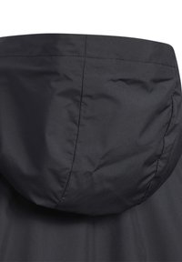 Chaqueta negra impermeable con una textura suave y mate, que cuenta con capucha y un diseño minimalista. Interior forrado con un sutil detalle de costura.