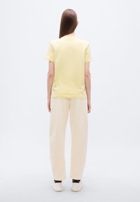 Κίτρινη βαμβακερή μπλούζα με κοντά μανίκια, συνδυασμένη με κρεμ φόρμα. Το σύνολο έχει άνετη εφαρμογή και ομαλές υφές.