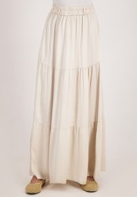 Lichtbeige maxi rok gemaakt van zachte, vloeiende stof. Voorzien van een elastische tailleband, gelaagde structuur en subtiele stikdetails.