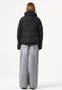 Schwarze Pufferjacke mit einem kurzen Design, hoher Kragen und elastischem Saum. Kombiniert mit weit geschnittenen hellgrauen Jeans.