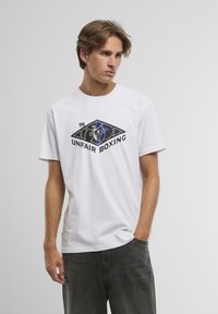 Balts kokvilnas T-krekls ar melnu un zilu grafiku, kurā ir teksts "UNFAIR BOXING". Īsas piedurknes un klasiska apaļa kakla izgriezums.