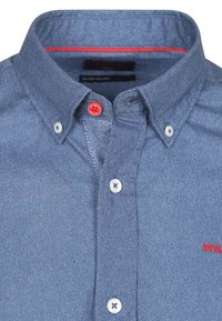 Blauw overhemdd met een gestructureerde stof. Bevat rode accenten knopen en een contrasterende rode binnenkraag. Witte knopen op de mouwen.