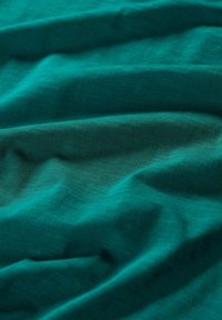 Turquoise bavlněná tkanina s hladkou texturou, vykazující jemné záhyby a subtilní variace v barvě a světle.