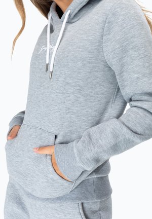 Sudadera de forro polar gris claro con bolsillo tipo canguro, puños y dobladillo acanalados, y cordones blancos. Presenta un sutil logo bordado en el pecho.