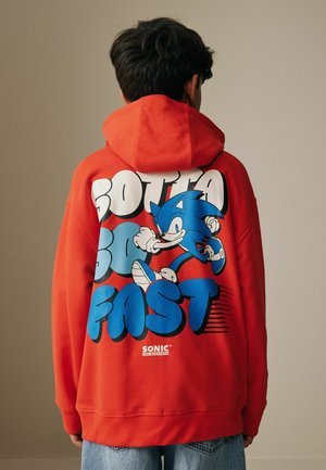 Person wearing a red hoodie with Sonic the Hedgehog running and "Gotta Go Fast" text on the back, paired with blue jeans.