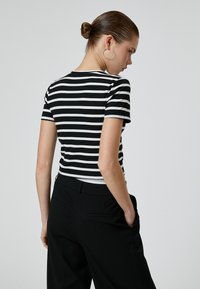 Camiseta ajustada de rayas en blanco y negro con mangas cortas, textura acanalada y cuello redondo, combinada con pantalones negros de cintura alta.