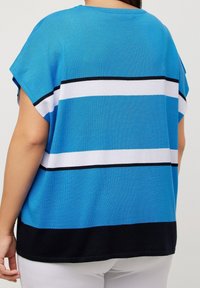 Modrý pletený top s vodorovnými pruhy světle modré, bílé a tmavě modré barvy. Má volný střih a krátké rukávy.