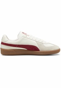 Białe sneakersy z czerwonym zamszowym akcentem, teksturowaną gumową podeszwą i sznurowanym designem; mają wyściełany kołnierz i wyszywane detale po bokach.