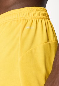 Gule meshshorts med elastisk talje og et synligt logo "DRYCELL". Stoffet har et struktureret mønster og sidelomme.