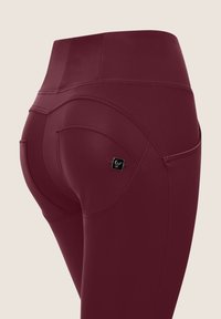 Leggings bordeaux a vita alta con una texture liscia, caratterizzati da dettagli di cucitura curvi e un piccolo logo vicino alla tasca.