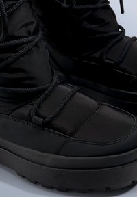 Schwarze Wanderschuhe mit einer Kombination aus glattem synthetischem Material und gepolstertem Nylon, mit strukturierten Sohlen und schwarzen Schnürsenkeln für sicheren Halt.