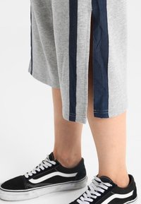 Grå sportshorts med marinblå ränder längs sidorna, med sidofickor. Matchat med svarta sneakers med vita detaljer.