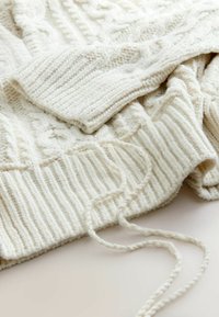 Siltā krēma krāsas adīts džemperis ar ribotām piedurknēm un apakšmalu, ar strukturētu rakstu un brīvām diegam pievienotu detaļu.