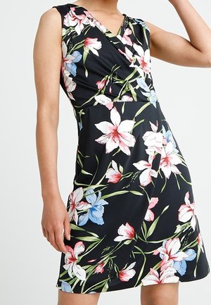 Ärmelloses schwarzes Kleid mit pinkem, weißem und blauem Blumenmuster und V-Ausschnitt an einer stehenden Person.