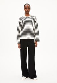 Zwart-wit gestreept shirt met lange mouwen, gecombineerd met zwarte broek met wijde pijpen en witte instapschoenen. Gladde stof en losse pasvorm.