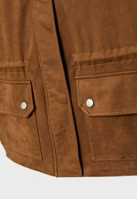 Section d'une veste en daim marron montrant deux poches avant à rabat avec des boutons-pression en argent et un laçage détaillé sur une surface en tissu lisse.