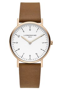 Montre avec bracelet en cuir marron, cadran blanc, boîtier doré, marqueurs d'heure noirs et aiguilles argentées. Nom de la marque "LIEBESKIND" affiché.
