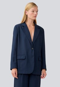Navy blazer with a single button closure, two front pockets, notched lapels, and a relaxed fit. Smooth fabric with minimal texture.