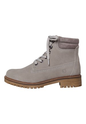 Bottine en suède gris avec un col rembourré, des lacets ronds, des œillets en métal et une semelle en caoutchouc avec une accentuation marron. Présente un détail de logo sur le côté.