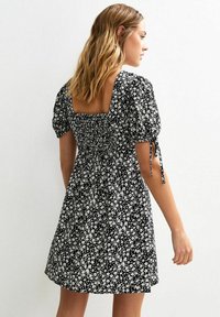 Vestido negro de flores con mangas cortas abullonadas, escote cuadrado y cuerpo fruncido. Presenta una falda acampanada y lazos en las mangas.