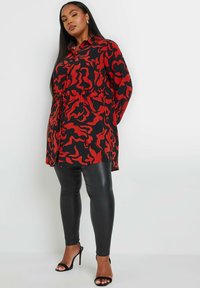 Abito camicia a righe rosse e nere con vita legata, abbinato a leggings in pelle nera e sandali con tacco alto. Tessuto morbido e stampa audace.