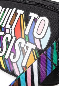Borsa in tessuto nera con una tipografia audace e multicolore che recita "PROGETTATA PER RESISTERE" e una tracolla a strisce colorate. Superficie testurizzata.