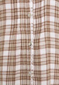 Brązowa i biała koszula w kratę zapinana na guziki, z metalowymi guzikami, teksturowanym materiałem oraz kontrastowym przeszyciem wzdłuż klapy guzików.