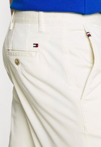 Lyse beige bomuldsshorts med en baglomme med knaplukning og et lille broderet logo i rød, hvid og blå.