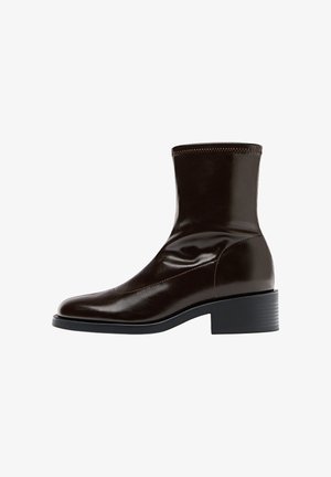 Brązowa skórzana botka za kostkę o gładkim wykończeniu, kwadratowym nosku, teksturowanym przeszyciem i niskim blokowym obcasie. Posiada elegancki, minimalistyczny design.
