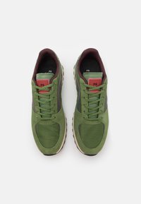 Ein Paar grüne Schnürsneakers mit Obermaterial aus Wildleder und Mesh, roten Logopatches auf den Zungen und beigen Gummisohlen, von oben betrachtet.