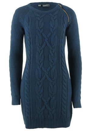 Femme portant une robe-pull bleu torsadé, des leggings noirs, des bottines bleues et un sac bandoulière noir.