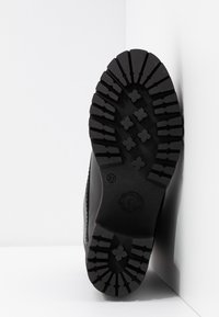 Semelle de botte en caoutchouc noire avec un dessin profond de crampons, comprenant des formes croisées et en losange pour l'adhérence. Taille 37 indiquée sur la semelle.