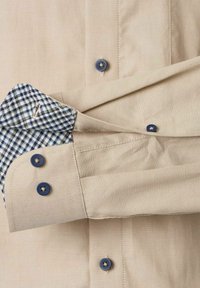 Beige Hemd mit blauen Knöpfen und einem karierten Innenfutter in Blau und Weiß an den Ärmeln, aus glattem Stoff mit strukturierter Gestaltung.
