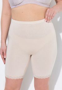 Un short beige en tissu lisse avec une taille haute et un bord en dentelle, offrant une silhouette ajustée.