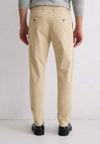 Beige Chinos aus Baumwolle mit geradem Schnitt, ausgestattet mit Gesäßtaschen mit Knopfverschlüssen und einer glatten Textur.