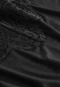 Fekete szövet bonyolult virágos csipke részlettel, amely a textúrát és a finom mintát mutatja puha hajtásokkal az anyagon.