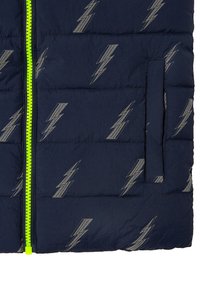 Tummansininen puffervest, jossa on vaaleanharmaa sahalaitakuviot, kirkkaan neonvihreä vetoketju ja sivutasku.