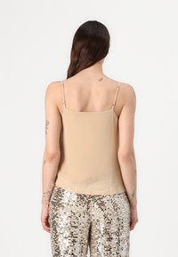 Beige camisole with thin adjustable straps, smooth texture, and a straight cut, paired with sequined pants featuring metallic accents.