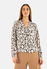 Blusa de manga larga en crema con un patrón floral negro, con cierre de botones en la parte delantera y un corte relajado. Textura de tela suave.