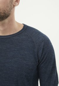 Tummansininen pitkähihainen paita, jossa on pyöreä pääntie ja raglan-hihat. Paidan kangas on pehmeää ja tekstuurista, ja siinä on hienovarainen heathered-kuvio.