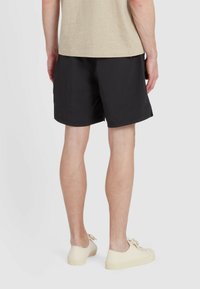 Pantaloni corti neri casual con una texture liscia, fascia elastica in vita e vestibilità rilassata, abbinati a sneakers chiare.