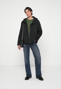 Czarna lekka kurtka z kapturem, noszona na zielonym swetrze. Niebieskie dżinsy w szerokim kroju i czarne buty. Prosty design, bez wyraźnych wzorów.