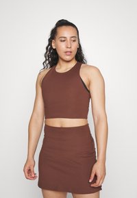Smeđa crop majica i odgovarajuća mini suknja izrađeni od rastezljivog materijala. Majica ima okrugli izrez i bez rukava.